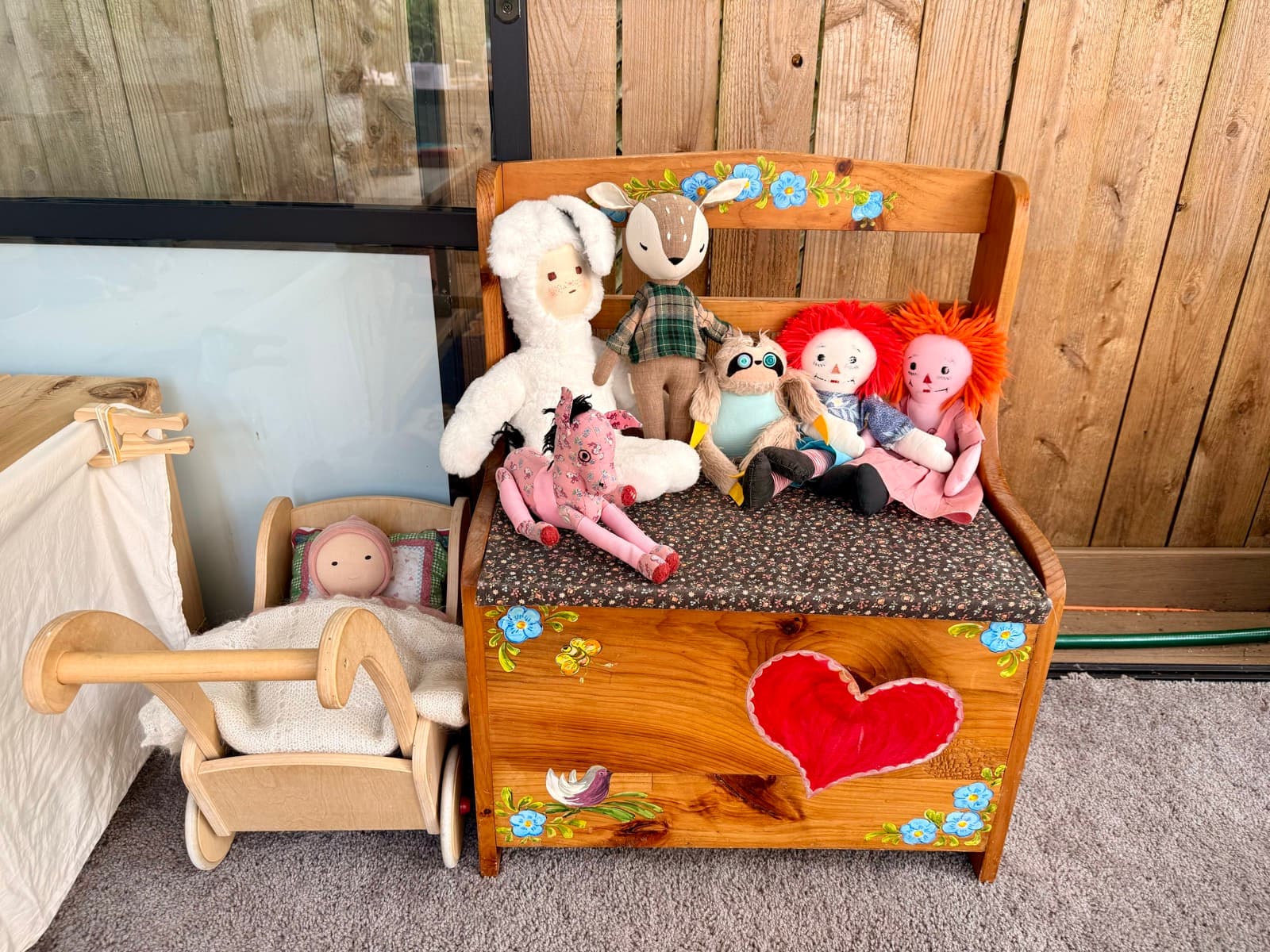 Handmade dolls and stuffed animals arranged on a painted toy bench