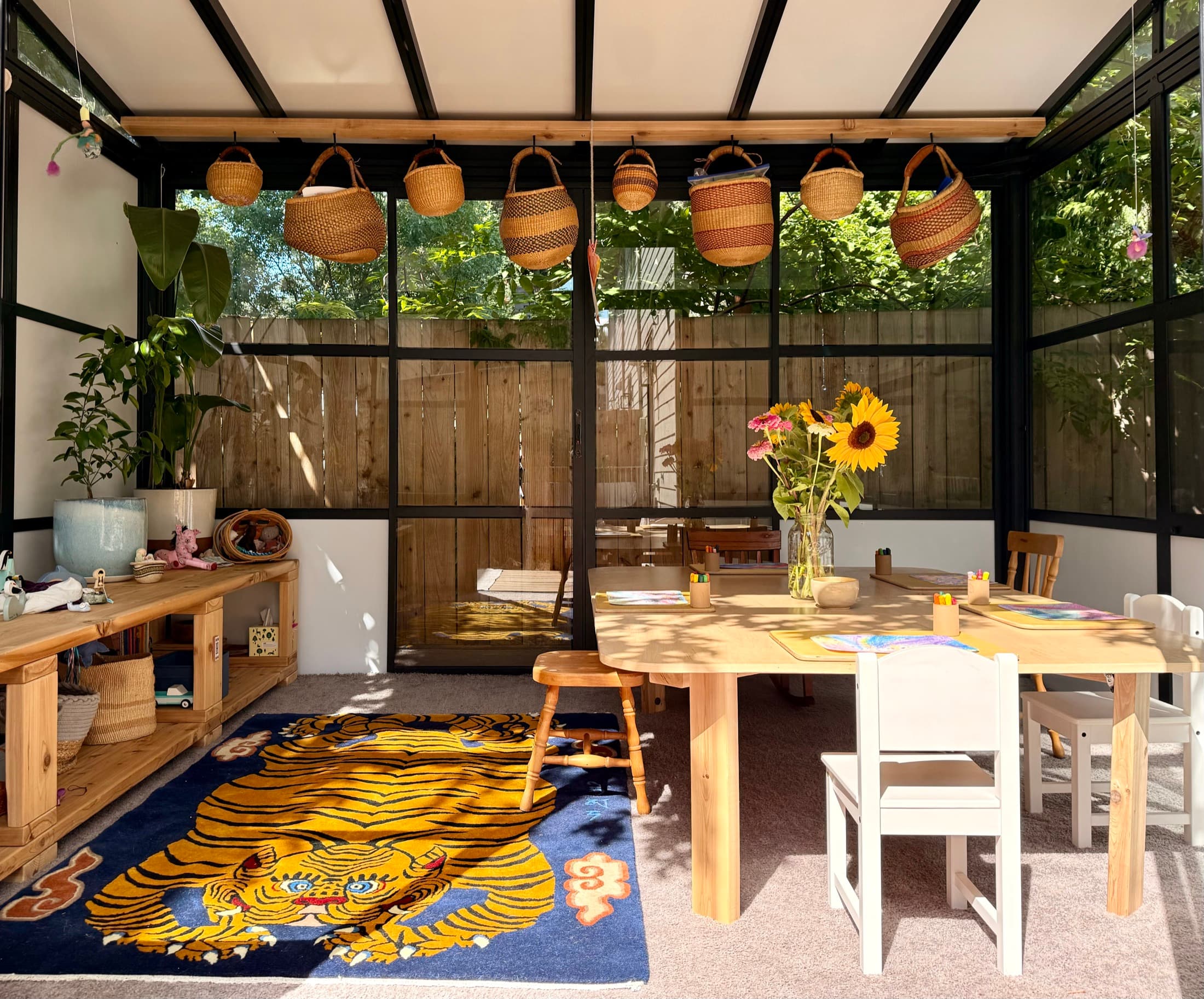 The sunlit studio, with hanging baskets, a table set for class with fresh sunflowers, and the tiger rug